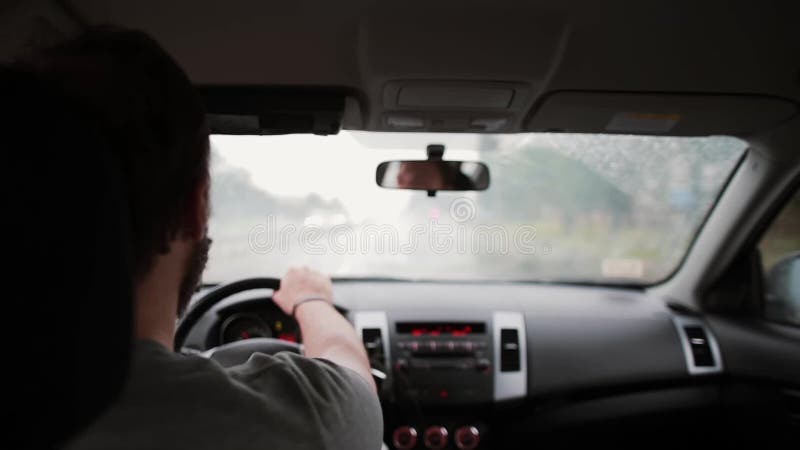 En tillbaka sikt av en man som kör en bil i regnet Händer på ett styrninghjul, arbeta för torkare