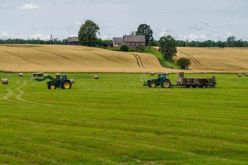 En traktor laddar baler av hö på en släp från en annan traktor fotografering för bildbyråer En traktor laddar baler av hö på en släp från en annan traktor fotografering för bildbyråer