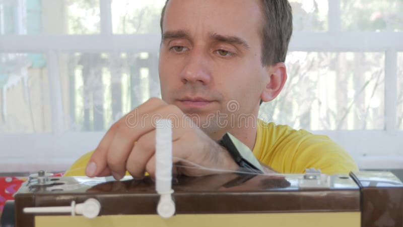 En trevlig man sitter på den elektriska symaskinen hemma Han syr flera lager av tyg och tjänar som ett funktionsdugligt hjälpmede