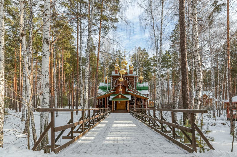 En träbro över en snöbana leder till en träkyrka i Ganina Yama i Yekaterenburg i Ryssland arkivfoton