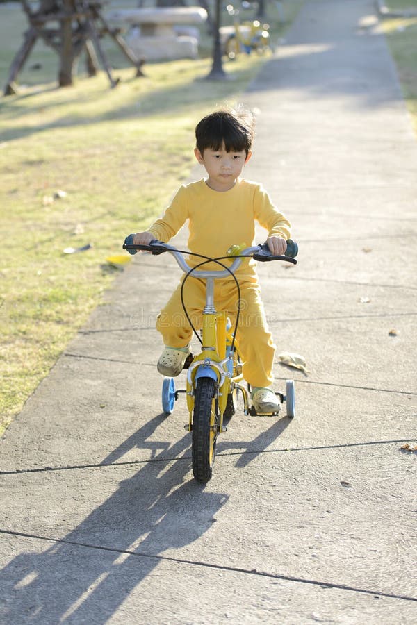 En underbar pojke som kör en cykel på en utomhuspark på morgonen. En porträttvärd, asiatisk pojke som kör en cykel på en utomhuspark på morgonen