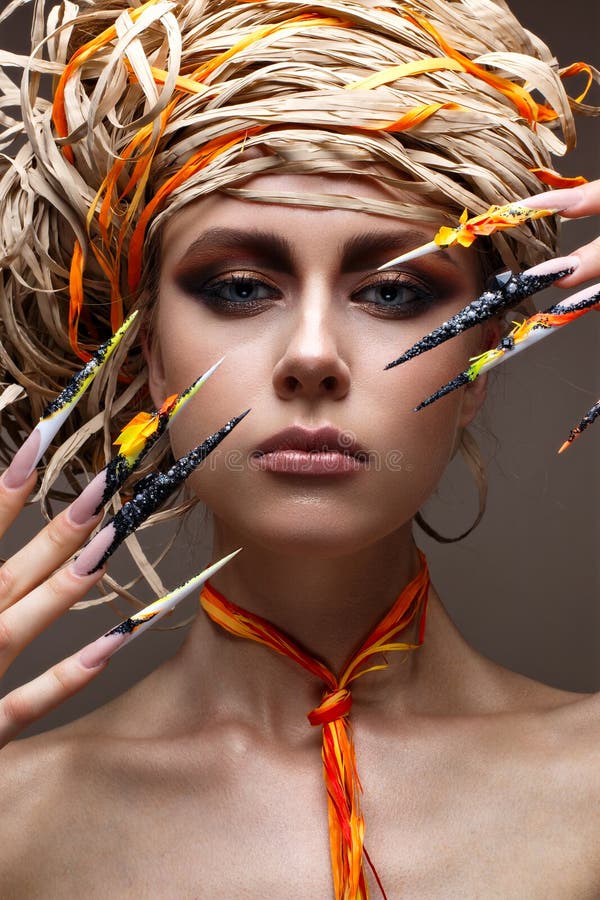 En ung flicka med länge dekorerat spikar och ljus idérik makeup Härlig modell med en sugrörhatt på hennes huvud Härlig manicur arkivfoton En ung flicka med länge dekorerat spikar och ljus idérik makeup Härlig modell med en sugrörhatt på hennes huvud Härlig manicur arkivfoton