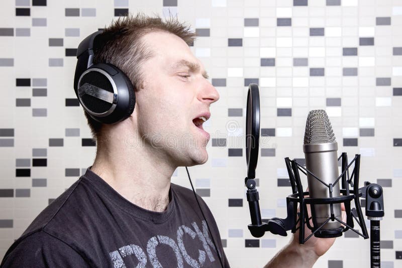 En ung grabbsångare och vaggar musikerallsånger i en studiokondensatormikrofon i hörlurar i en inspelningstudio fotografering för bildbyråer En ung grabbsångare och vaggar musikerallsånger i en studiokondensatormikrofon i hörlurar i en inspelningstudio fotografering för bildbyråer