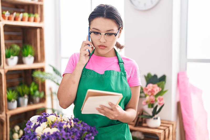 En ung historisk kvinna som floriserar och pratar på smartphone-läsbok på florist royaltyfri bild