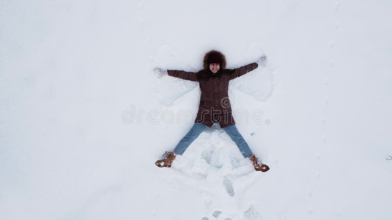 A young woman makes the figure of an angel in the snow. Top view of a woman from a drone. 4k. A young woman makes the figure of an angel in the snow. Top view of a woman from a drone. 4k