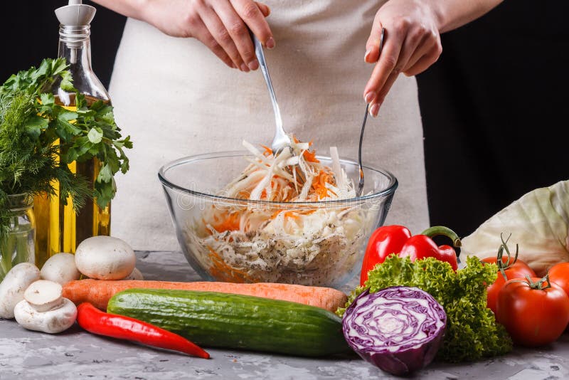 En ung kvinna i en grå apron blandar en sallad kål royaltyfri fotografi