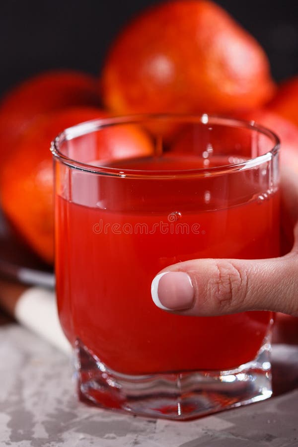 En ung kvinna i en grå apron tar ett glas juice blod orange royaltyfria foton