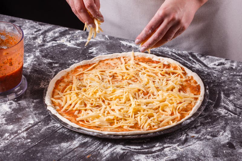 En ung kvinna i en grå aprong förbereder en pepperonpizza royaltyfri foto