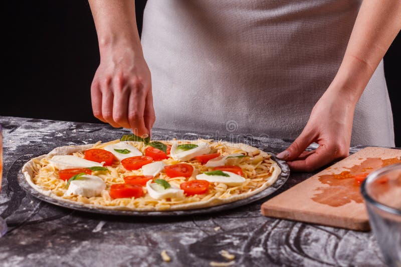 En ung kvinna i en grå aprong förbereder en pizza margarita royaltyfria bilder