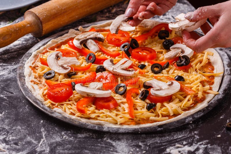 En ung kvinna i en grå aprong förbereder en vegetarisk pizza royaltyfri bild