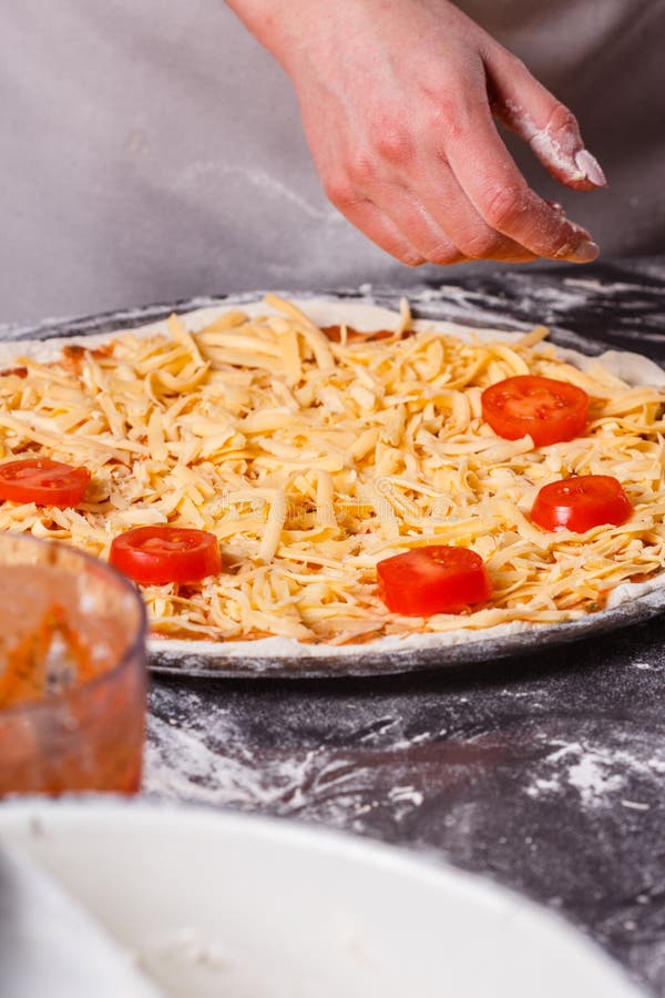 En ung kvinna i en grå aprong förbereder en vegetarisk pizza royaltyfria bilder