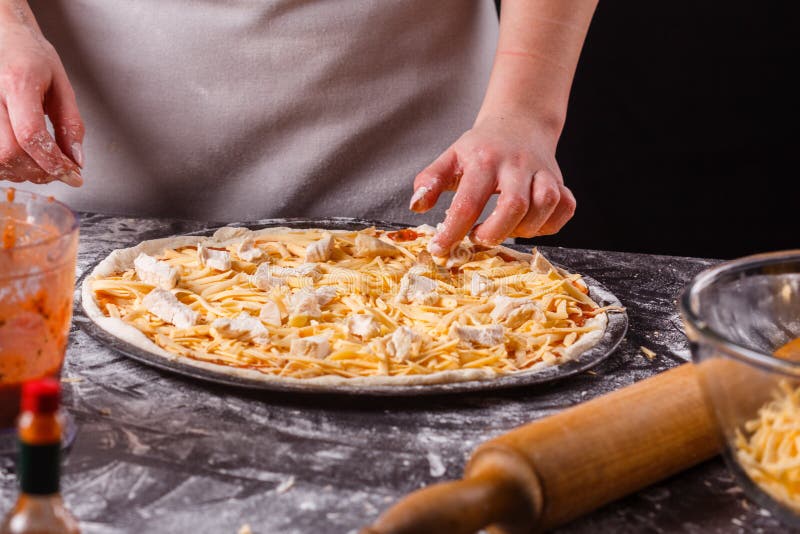 En ung kvinna i en grå aprons förbereder en Hawaiisk pizza royaltyfria bilder