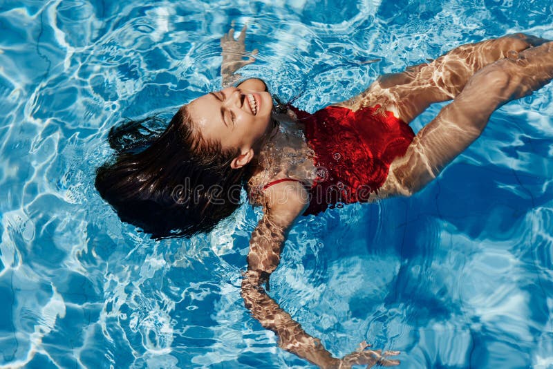 En ung kvinna i poolen i en röd baddräkt med ett vackert leende som ligger på vattnet och simmar i solen och simmar in i royaltyfri fotografi