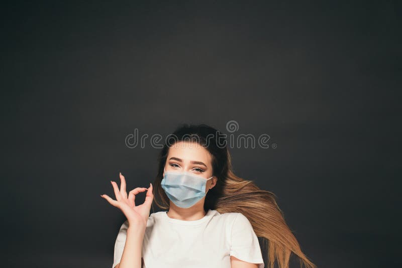 En ung kvinna i en skyddande medicinsk mask på ansikte på svart studio med toppvy visar en gest arkivfoto