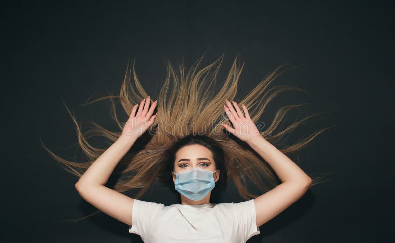 En ung kvinna i skyddande medicinsk mask på ansikte på svart studio, upphöjda händer som en gest av överlämnande royaltyfria foton