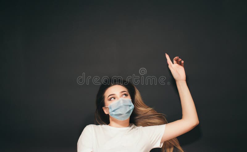En ung kvinna i en skyddande medicinsk mask på ansiktet på den svarta studion, en tjej med överblick på baksidan som skjuter upp e royaltyfri fotografi