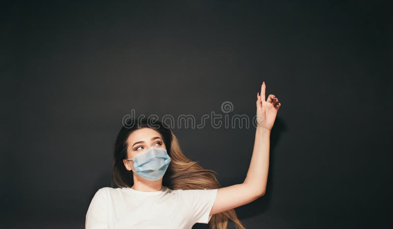 En ung kvinna i en skyddande medicinsk mask på ansiktet på den svarta studion, en tjej med överblick på baksidan som skjuter upp e royaltyfria foton