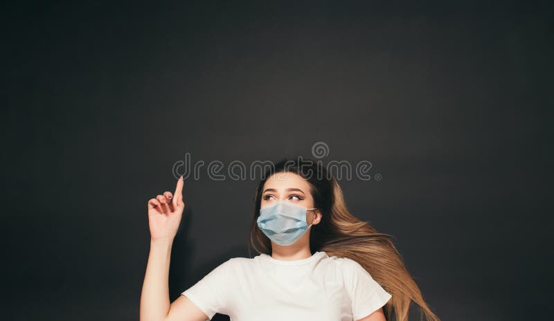 En ung kvinna i en skyddande medicinsk mask på ansiktet på den svarta studion, en tjej med överblick på baksidan som skjuter upp e arkivfoton