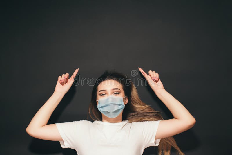 En ung kvinna i en skyddande medicinsk mask på ansiktet på den svarta studion, en tjej med överblick på baksidan som skjuter upp e royaltyfri foto