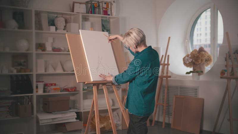 En ung kvinna med kort hårskiss på arbetsytan och lyssna på musik i hörlurarna