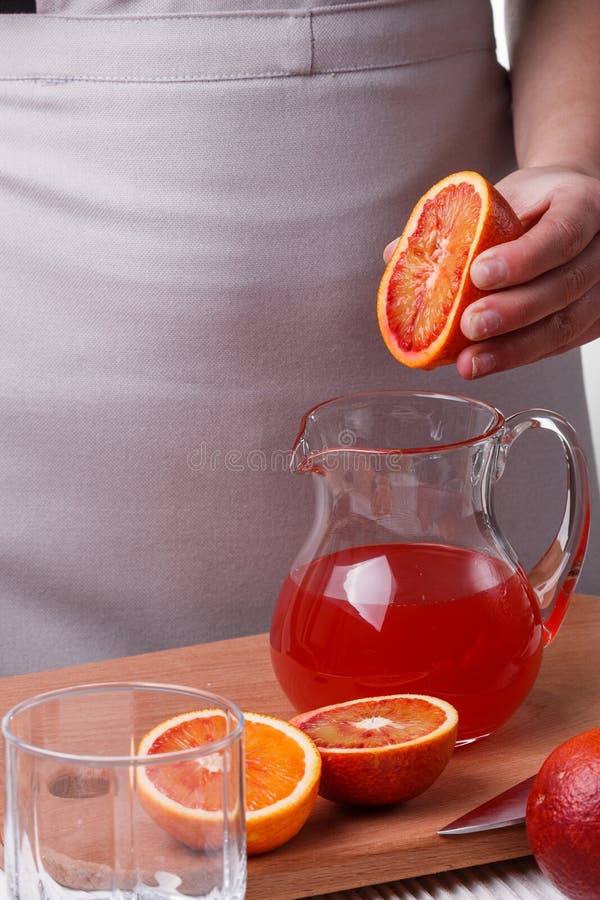 En ung kvinna på en grå apron klämmer juice av orange blod royaltyfri bild