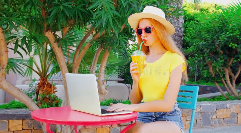 En ung kvinna som arbetar med bärbar dator och dricksaft medan hon sitter vid bordet på sommarsemestern