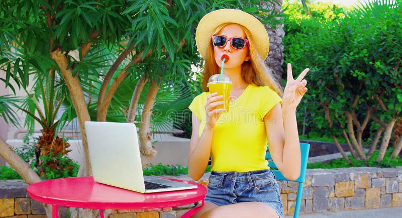 En ung kvinna som arbetar med bärbar dator och dricksaft medan hon sitter vid bordet på sommarsemestern