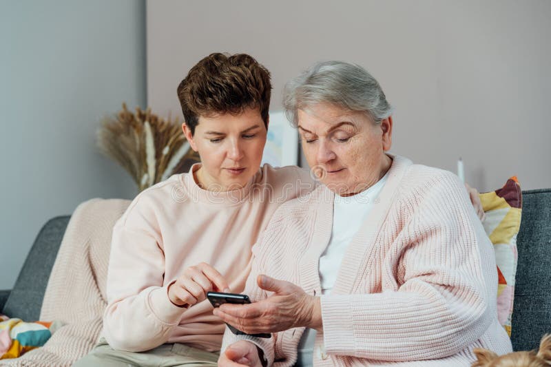 En ung kvinna som förklarar sin äldre mor eller morma hur hon använder smartphone. Pensionerad dam som upptäcker mobil teknik arkivbilder