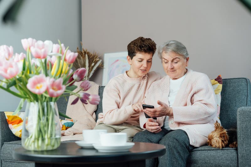 En ung kvinna som förklarar sin äldre mor eller morma hur hon använder smartphone. Pensionerad dam som upptäcker mobil teknik arkivbild