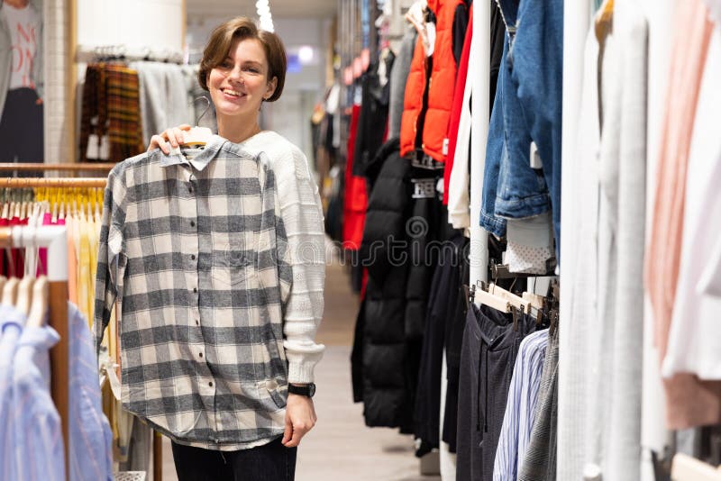 En ung kvinna som försöker på en stilig plaid-skjorta i en klädaffär arkivbilder