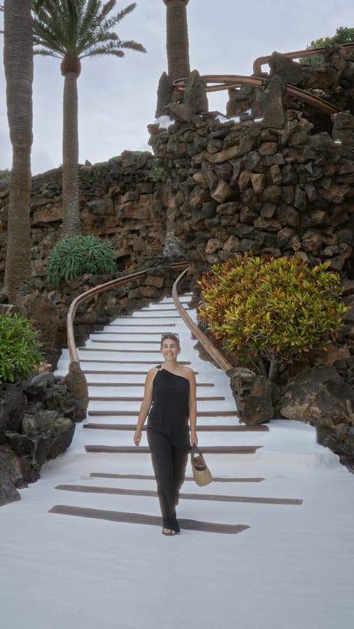 En ung kvinna som går nedför de vita stenstegen mitt i spolväxterna och det klippiga landskapet vid jameos del agua lanzarote kana royaltyfri fotografi