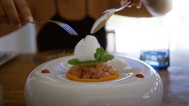 En ung kvinna som har gourmetmjöl i en fin restaurang inomhus, som använder gaffel och sked för att hugga en exquisitionsrätt royaltyfri fotografi