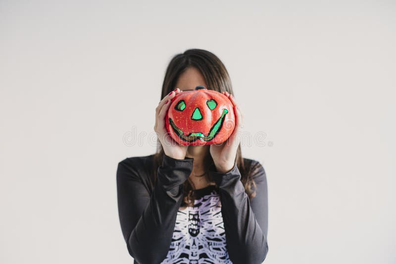 En ung kvinna som håller en pumpa som täcker hennes ansikte Med ett svart och vitt skelett Halloween-koncept Inomhus livsstil royaltyfri fotografi
