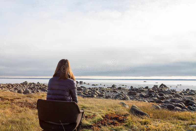En ung kvinna som ser den steniga stranden som bara sitter i en stol royaltyfria foton En ung kvinna som ser den steniga stranden som bara sitter i en stol royaltyfria foton