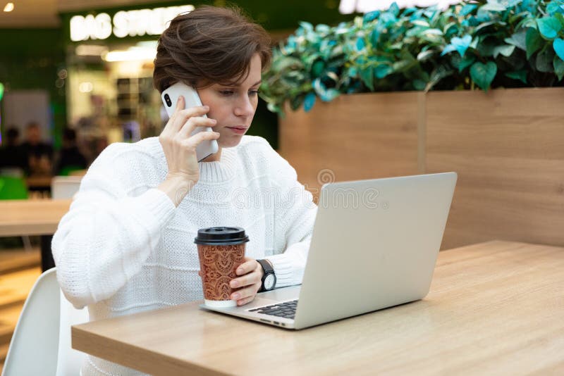 En ung kvinna som söker ett jobb som ringer upp lediga platser på telefonen och tittar på en bärbar dator fotografering för bildbyråer