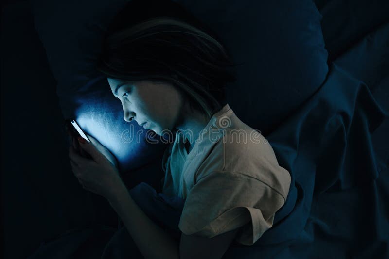 En ung kvinna tittar på sociala nätverk på sin telefon på natten eller svarar på ett meddelande. översta vyn. arkivbild En ung kvinna tittar på sociala nätverk på sin telefon på natten eller svarar på ett meddelande. översta vyn. arkivbild