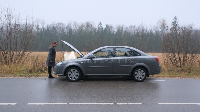 En ung kvinna en trasig bil och öppnar huven i skogen.