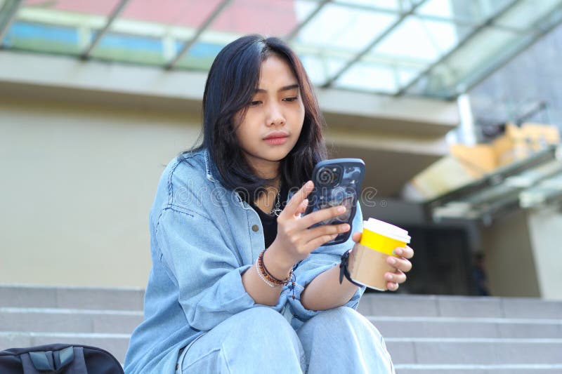 En ung kvinnlig digital nomad som använder smartphone på allvar och dricker en kopp kaffe i sociala medier och video arkivfoton