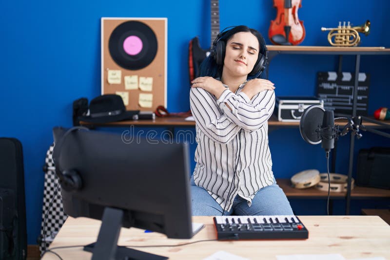 En ung modern flicka med blått hår i musikstudion med hörlurar som kramar sig själv glad och positiv och självbelåten royaltyfri bild