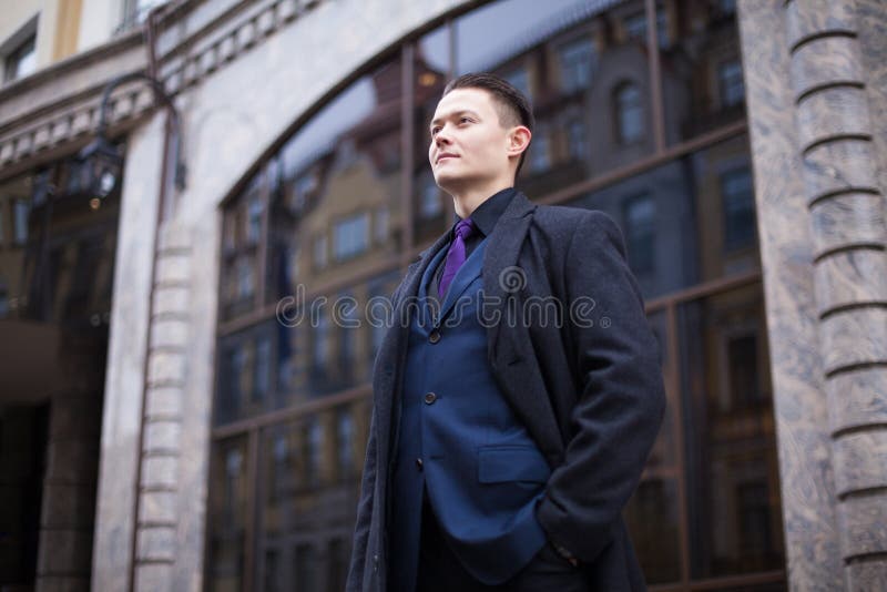 En ung och målinriktad bankman i en blå kostym och rock ser fram emot bankbyggnaden royaltyfri fotografi En ung och målinriktad bankman i en blå kostym och rock ser fram emot bankbyggnaden royaltyfri fotografi