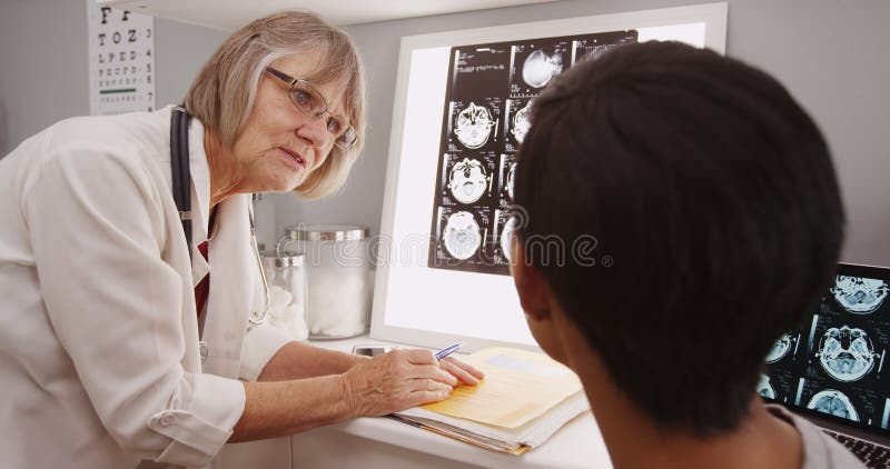 En ung patient som konsulterar med en hög doktor royaltyfri fotografi En ung patient som konsulterar med en hög doktor royaltyfri fotografi