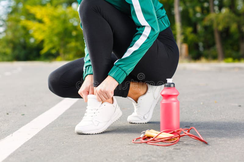 En ung sportig kvinna binder upp skosnöre på gymnastikskor En flicka med den perfekta kroppen som gör övningar arkivbilder En ung sportig kvinna binder upp skosnöre på gymnastikskor En flicka med den perfekta kroppen som gör övningar arkivbilder