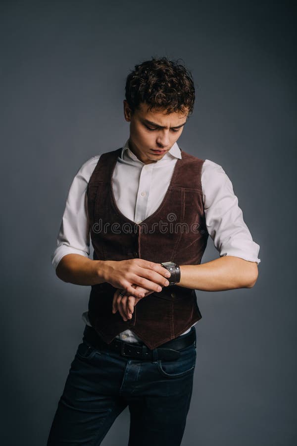 En ung stilig grabb som poserar på en grå studiobakgrund Mannen är stilfull och elegantly iklädd jeans, en skjorta och arkivfoton En ung stilig grabb som poserar på en grå studiobakgrund Mannen är stilfull och elegantly iklädd jeans, en skjorta och arkivfoton