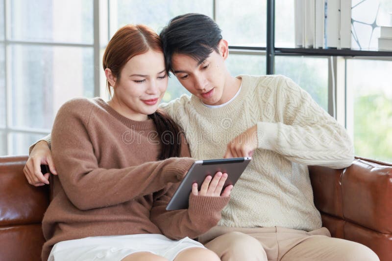 En ung, stilig pojkvän och en vacker kvinnlig flickvän som leker på soffa med hjälp av datorshopping online arkivfoto