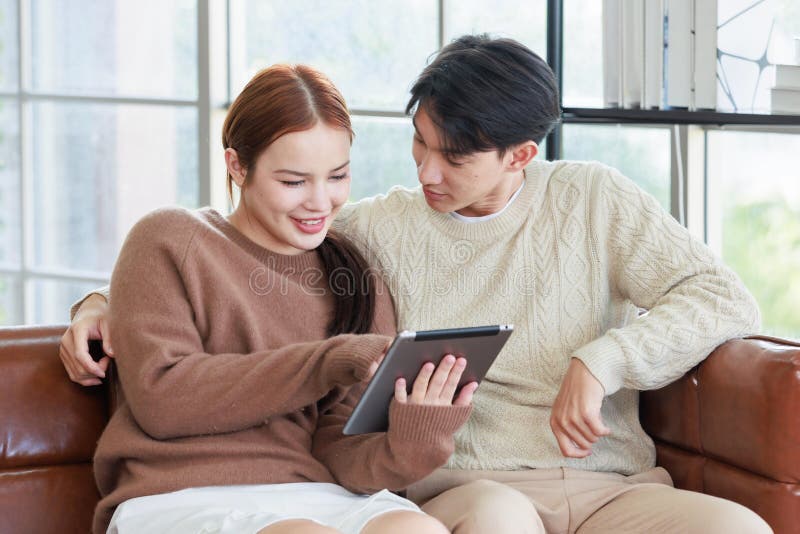 En ung, stilig pojkvän och en vacker kvinnlig flickvän som leker på soffa med hjälp av datorshopping online fotografering för bildbyråer