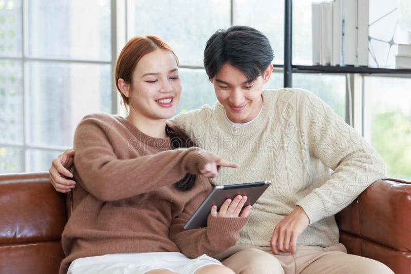 En ung, stilig pojkvän och en vacker kvinnlig flickvän som leker på soffa med hjälp av datorshopping online royaltyfria foton