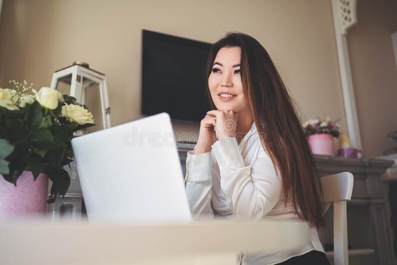 En ung, vacker affärskvinna som arbetar online med en bärbar dator placerad vid bordet på hemkontoret. leende royaltyfria foton