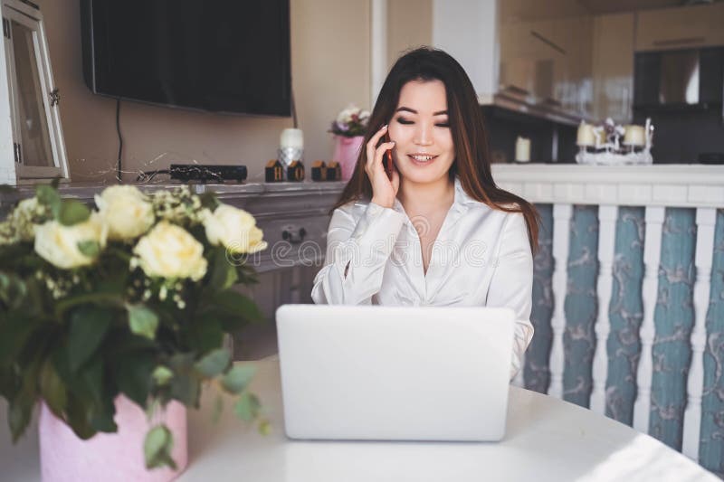 En ung, vacker affärskvinna som arbetar online med en bärbar dator placerad vid bordet på hemkontoret. leende royaltyfri fotografi