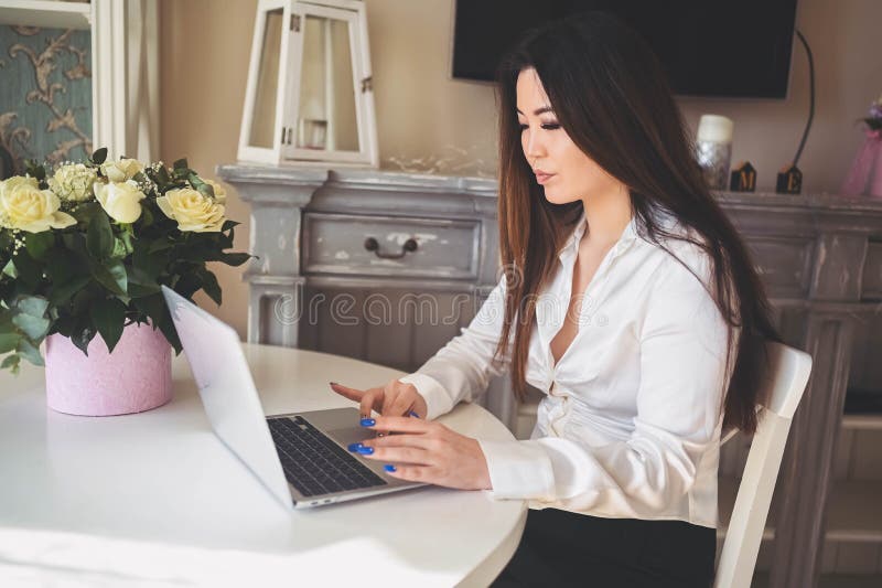En ung, vacker affärskvinna som arbetar online med en bärbar dator placerad vid bordet på hemkontoret. leende royaltyfri bild