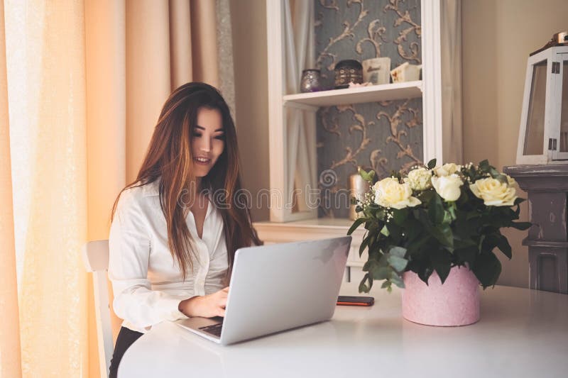 En ung, vacker affärskvinna som arbetar online med en bärbar dator placerad vid bordet på hemkontoret. leende royaltyfria bilder